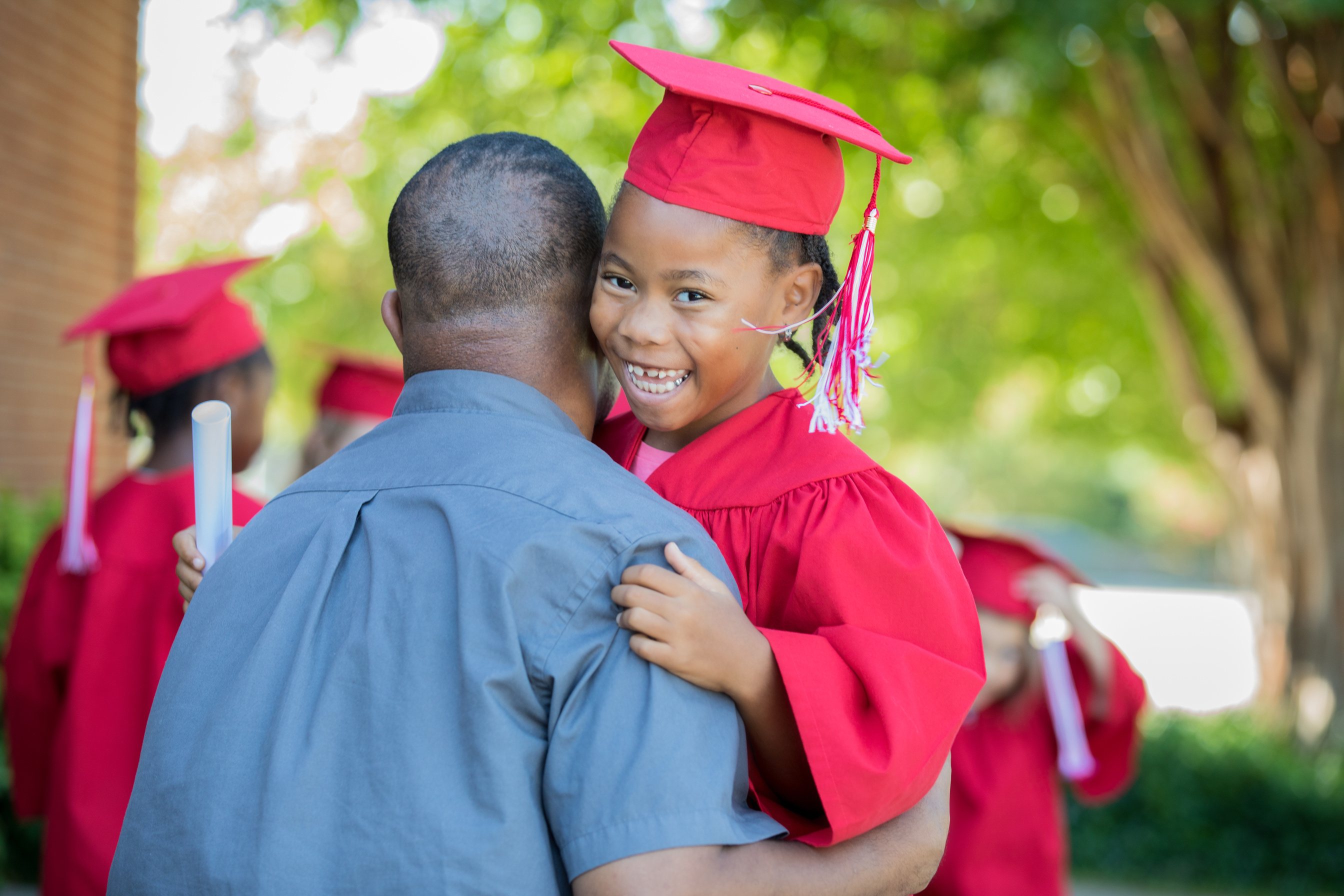 Adorable little girl embraces father after kindergarten graduation